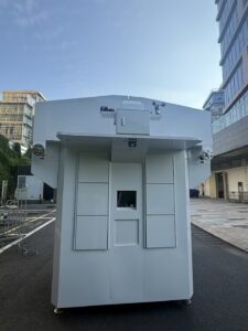 Large white outdoor industrial imaging cabinet with a small front window and top-mounted sensors/sirens.